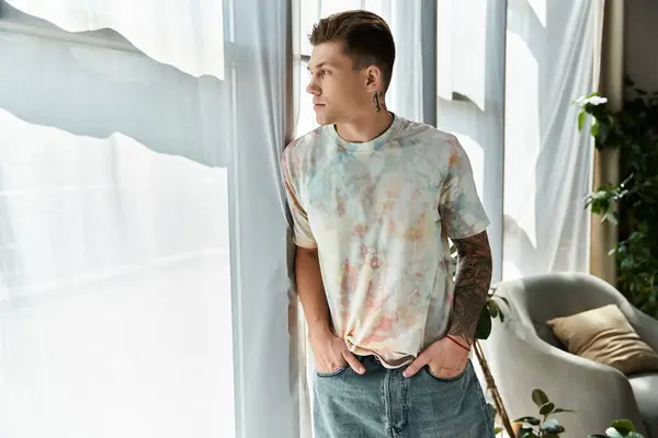Handsome young man stands by the window, lost in deep thought during daytime. — Stock Photo