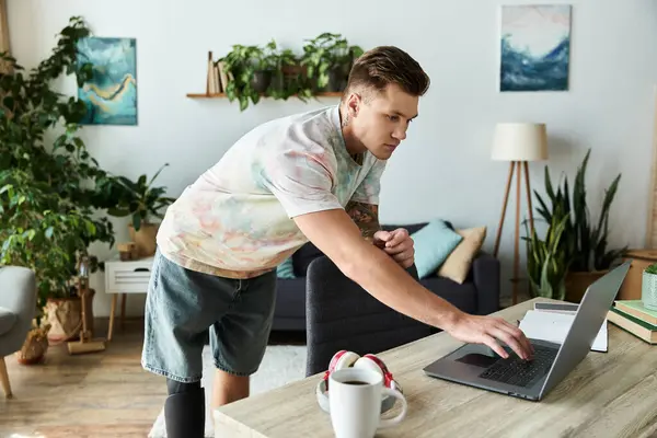 Young man with a prosthetic leg focuses on his laptop in a vibrant living room surrounded by plants. — Stock Photo