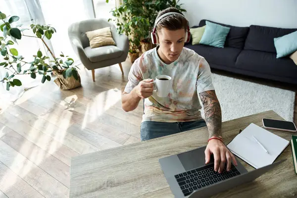 Um jovem gosta de café enquanto trabalha em seu laptop em casa. — Fotografia de Stock