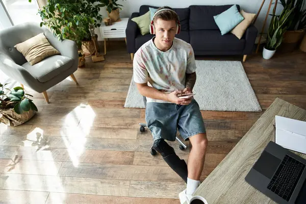 Stylish youth sits in a lively room, listening to music while using a smartphone and chair. — Stock Photo