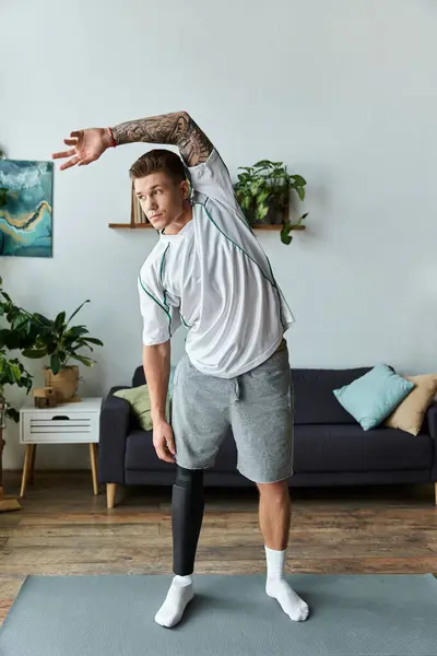 A young man with a prosthetic leg stretches in a bright living room with greenery around him. — Stock Photo