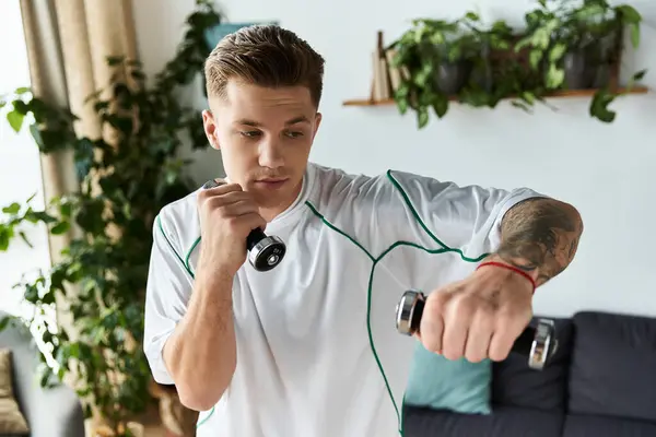 Young man trains indoors, lifting dumbbells with a determined focus on fitness. — Stock Photo