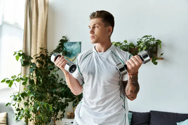 A handsome young man is engaged in strength training with dumbbells at home. — Stock Photo