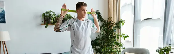 A young man confidently works out at home with a resistance band, showcasing his fitness. — Stock Photo