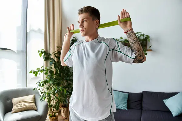 Focused young man performs strength exercises using a resistance band in a bright living room. — Stock Photo