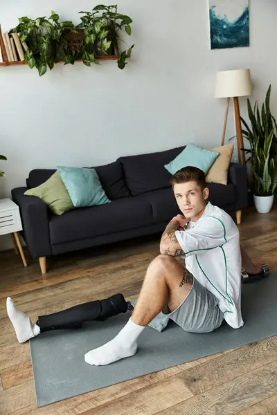 A young handsome man sits on a mat, looking thoughtful, in a modern living room filled with plants. — Stock Photo