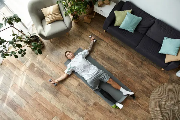 A young man with a prosthetic leg practices stretching on a mat at home, amid plants. — Stock Photo