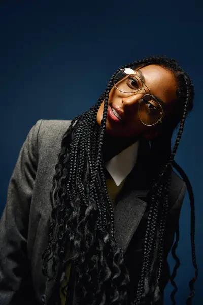 Confident young woman with long braids and glasses poses in a vibrant setting. — Stock Photo
