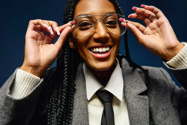 A young woman with braids smiles brightly while adjusting her glasses in a trendy outfit. — Stock Photo