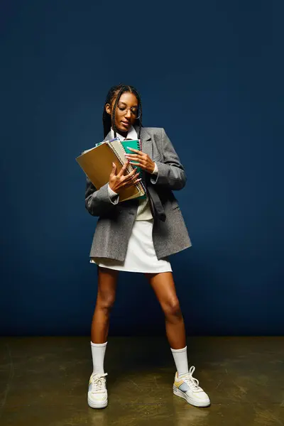 A beautiful young woman stands confidently, clutching a folder and beverage while dressed stylishly. — Stock Photo