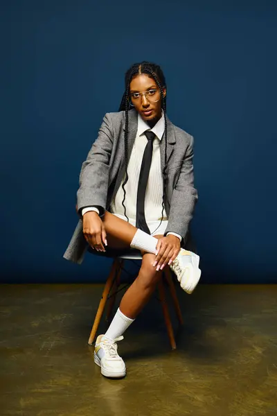 A young woman sits gracefully on a chair, wearing a trendy outfit with confidence and charm. — Stock Photo