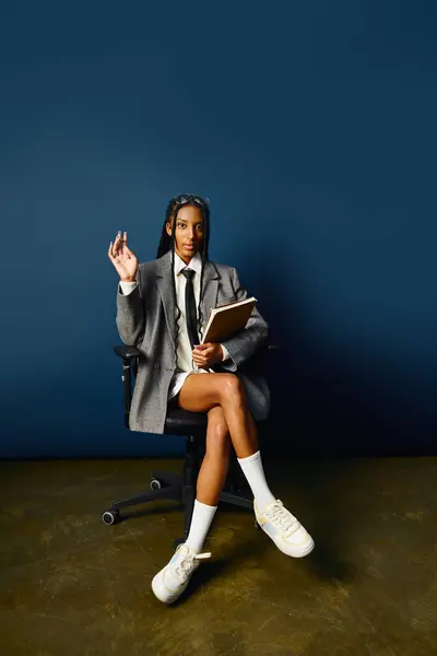A young woman in a grey blazer and white shirt sits confidently, holding a notebook. — Stock Photo