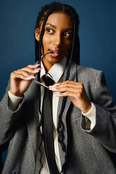 A confident young woman in a chic outfit adjusts her glasses, showcasing her braided hair. — Stock Photo