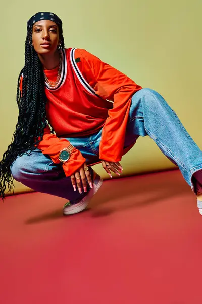 Bright colors highlight a stylish young woman squatting confidently against a geometric backdrop. — Stock Photo