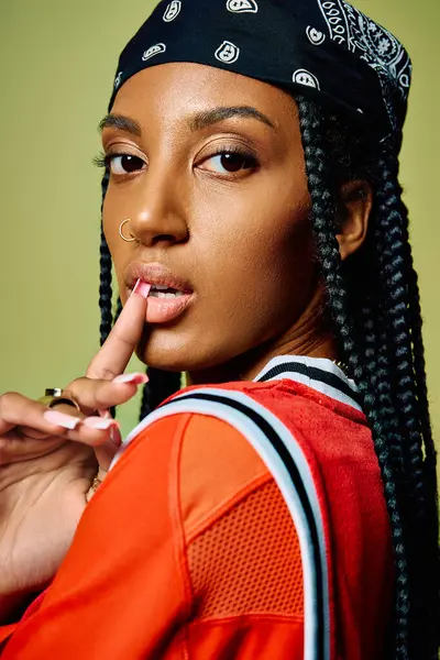 A confident young woman poses with her finger on her lips, flaunting braids and a chic outfit. — Stock Photo