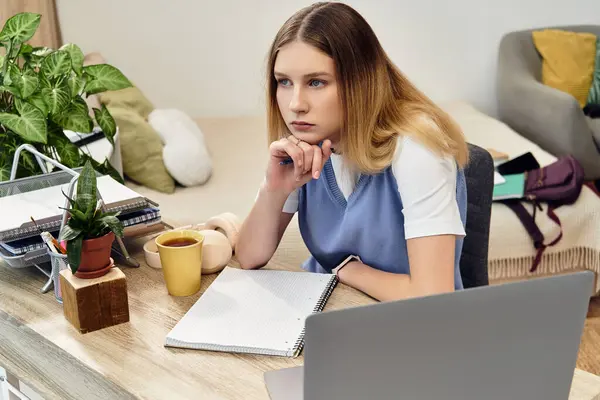 Una adolescente se sienta pensativamente en su mesa de estudio en una habitación acogedora, rodeada de decoración para el hogar. - foto de stock