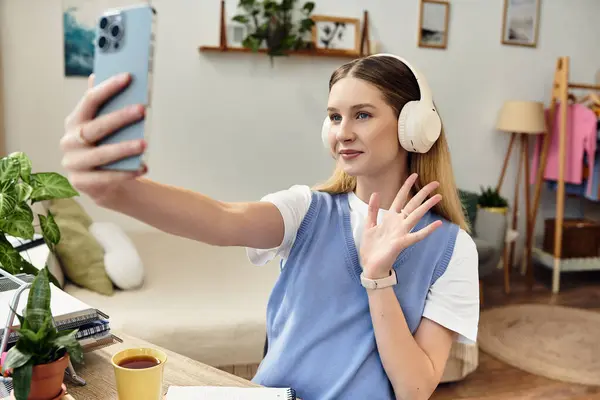 Uma linda adolescente gosta de uma videochamada, usando fones de ouvido e cumprimentando amigos em casa. — Fotografia de Stock