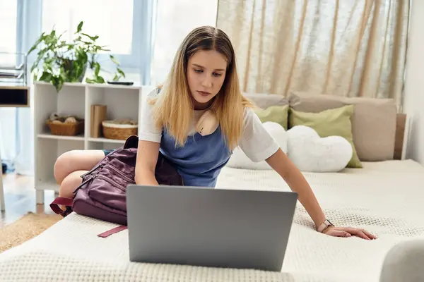 Adolescente assise sur son lit, concentrée sur son ordinateur portable, embrassant la culture moderne de la jeunesse à la maison. — Photo de stock