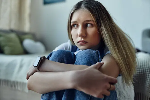 A pretty girl sits curled up in her room, lost in thought, surrounded by her daily life. — Stock Photo