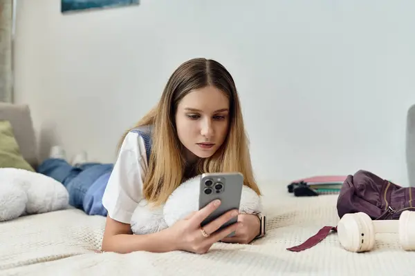 Молода дівчина лежить на своєму ліжку, всмоктується в її смартфон, в оточенні її особистого простору. — стокове фото