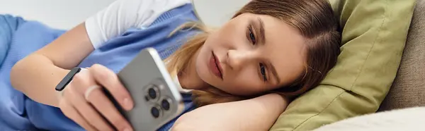 A pretty teenage girl relaxed on her bed, engaged with her smartphone in a modern room, banner — Stock Photo