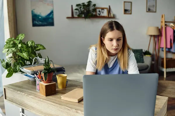 A teenage girl engages with her laptop in a stylish, welcoming bedroom, surrounded by plants. — Stock Photo