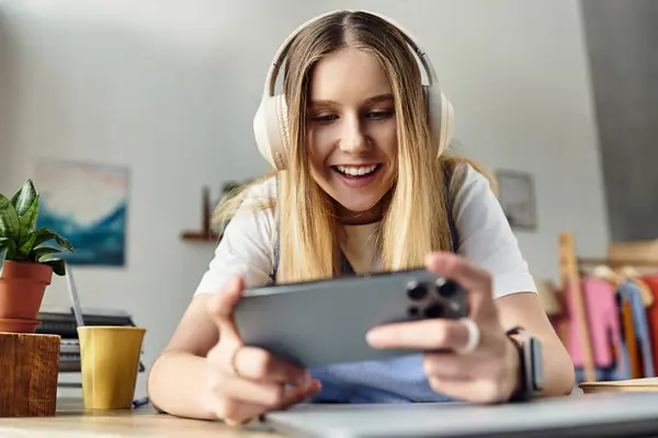 A cheerful teenage girl immersed in her favorite mobile game while lounging at home. — Stock Photo