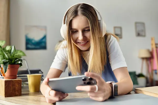 A cheerful teenage girl relaxes at home, absorbed in her smartphone while wearing headphones. — Stock Photo