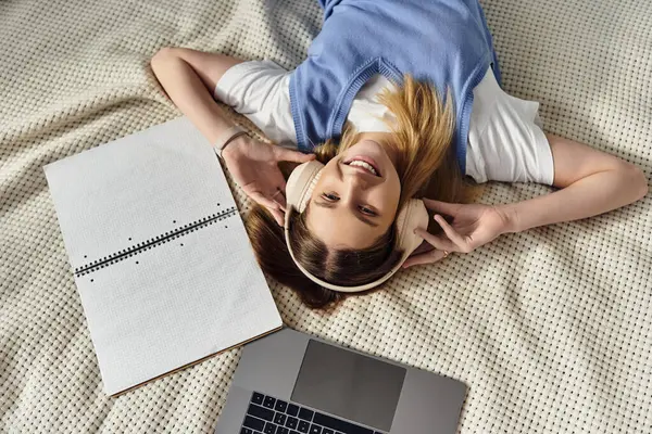 A cheerful teenage girl lies on her bed with headphones, immersed in her favorite tunes. — Stock Photo