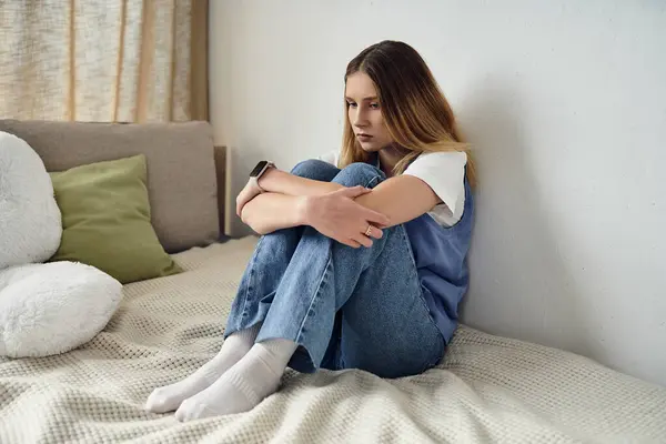 A teenager sits thoughtfully on her bed, surrounded by soft textures and light colors in her room. — Stock Photo