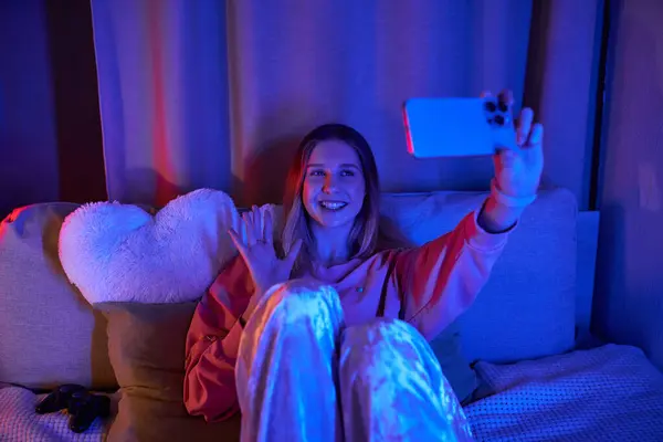 A cheerful teenage girl relaxes in her cozy room, capturing the moment on her phone. — Stock Photo