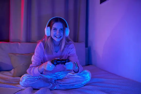 Una giovane ragazza si diverte a giocare ai videogiochi nella sua accogliente e colorata stanza durante la sera. — Foto stock