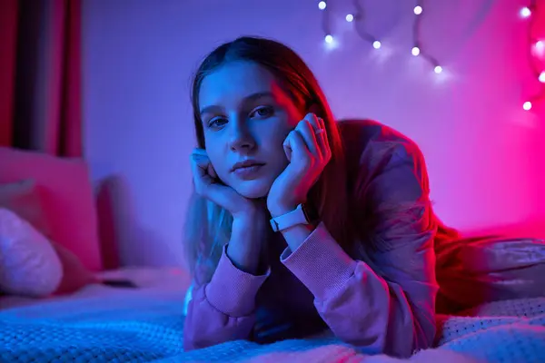 A teenage girl relaxes in her stylish room, surrounded by colorful lights in the evening. — Stock Photo