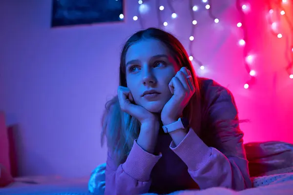 A teenage girl relaxes in her room, surrounded by colorful lights during the evening. — Stock Photo