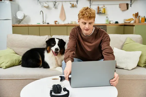 A young man with red hair interacts with his Australian Shepherd while using a laptop. — Stock Photo