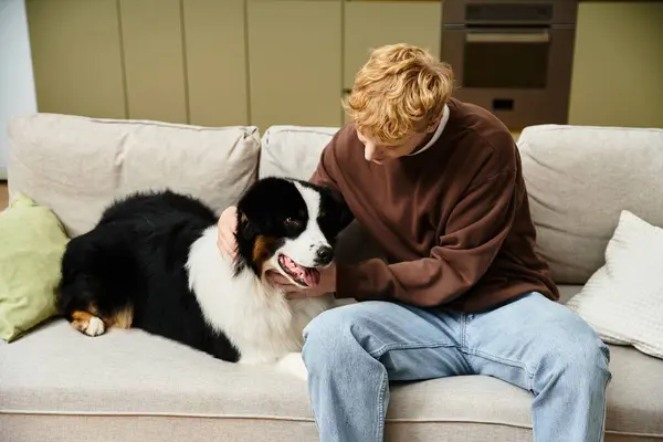 In a modern apartment, a young redhead man happily interacts with his cute Australian Shepherd. — Stock Photo