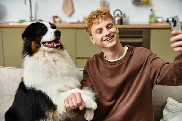 A young man with red hair shares a joyful moment with his Australian Shepherd in a modern apartment. — Stock Photo