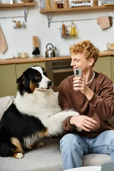 A cheerful young man with red hair shares a laugh with his cuddly Australian Shepherd at home. — Stock Photo