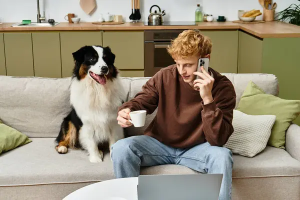 A young redhead man enjoys a cozy day at home with his Australian Shepherd by his side. — Stock Photo