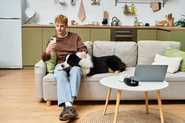 Relaxing at home, a young man with red hair uses his phone while his dog lounges beside him. — Stock Photo