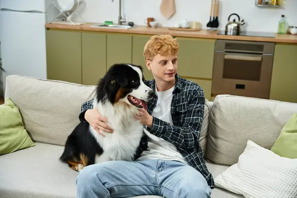 In a stylish apartment, a young redhead man sits with his adorable Australian Shepherd dog. — Stock Photo