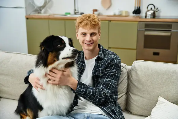 A cheerful young man with red hair plays with his Australian Shepherd dog in a cozy apartment. — Stock Photo