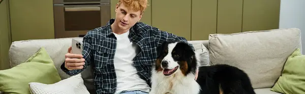 A young redhead man smiles while capturing a joyful moment with his Australian Shepherd, banner — Stock Photo