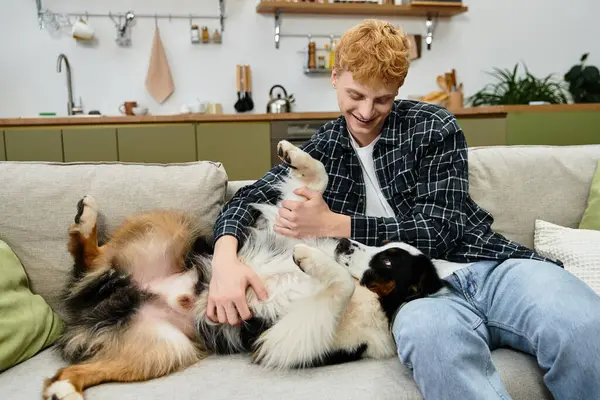 A young redhead man enjoys playful cuddles with his Australian Shepherd in a cozy apartment. — Stock Photo