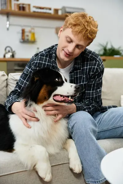 A young man with red hair lovingly interacts with his Australian Shepherd dog at home. — Stock Photo