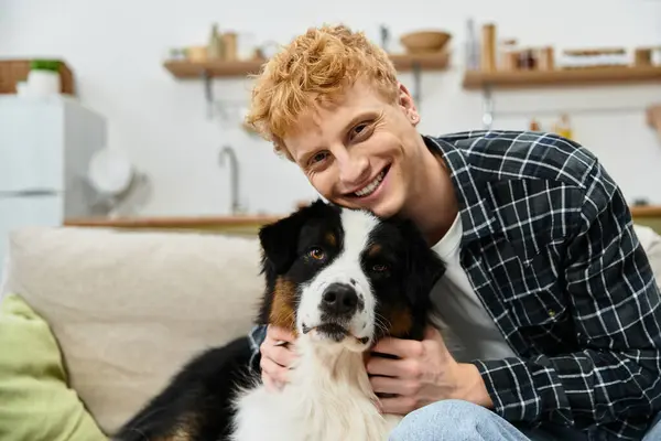 A young redhead man happily cuddles his Australian Shepherd, enjoying quality time at home. — Stock Photo