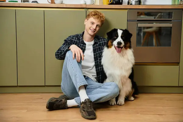 Ein junger Mann mit roten Haaren sitzt auf dem Boden neben seinem pelzigen Australian Shepherd in einem stilvollen Haus. — Stockfoto