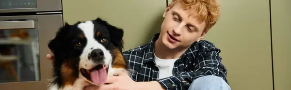 A young redhead man enjoys playful time with his happy Australian Shepherd dog at home, banner — Stock Photo