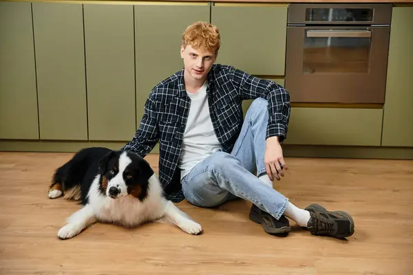 A young redhead man sits on the floor, bonding with his Australian Shepherd dog in a chic apartment. — Stock Photo