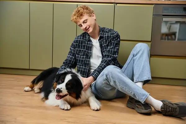 A cheerful young man pets his Australian Shepherd at home. — Stock Photo
